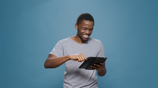 Adulto joven riéndose de la aplicación de medios sociales en tableta digital, navegando por Internet en la red en línea. Hombre sonriente que se siente alegre y escribe mensajes de texto en un dispositivo portátil con pantalla táctil.