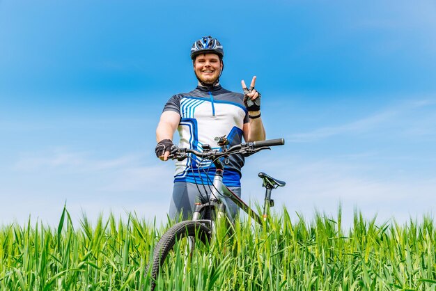 Adulto joven sonriente hombre de pie con bicicleta en cebada verde fi