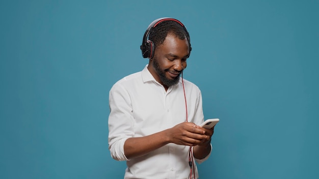 Adulto moderno usando fone de ouvido e smartphone para ouvir música, se divertindo com música de rádio e ritmo estéreo na frente da câmera. Homem confiante alegre ouvindo áudio mp3 em fones de ouvido.