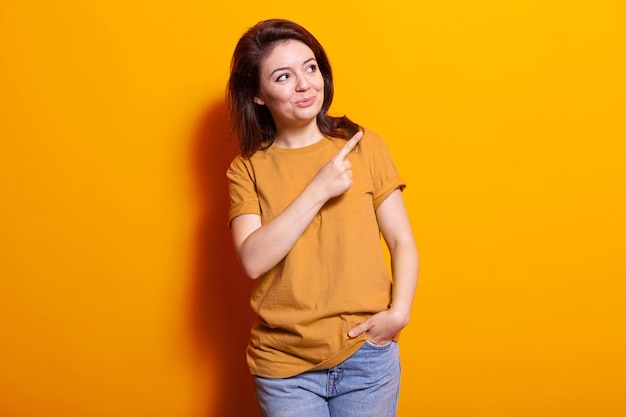 Adulto positivo que usa el dedo índice para señalar el lado derecho del estudio. Joven señalando a un lado y de pie sobre un fondo aislado mientras posa para la cámara. mujer caucásica sonriendo