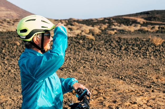 Un adulto y senior en una montaña rocosa montando en bicicleta haciendo ejercicio - mujer madura activa haciendo actividad y mirando el horizonte