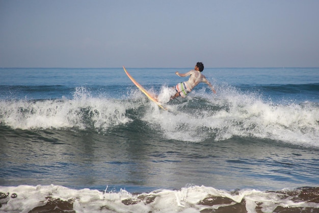 Adultos jóvenes atrapando olas surfeando en la costa oeste de Pangandaran en un día cálido y soleado en un claro bl