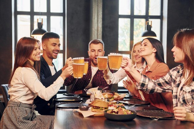 Adultos jóvenes Grupo de jóvenes amigos sentados juntos en el bar con cerveza