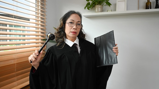 Advogada ou advogada juíza madura confiante em uniforme de roupão com martelo martelo martelo Lei e conceito de justiça