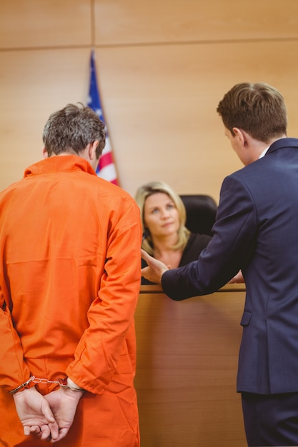 Foto advogado e juiz falando ao lado do criminoso algemado