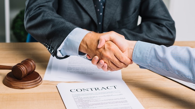 Advogado masculino que agita as mãos com o cliente sobre o papel do contrato na tabela