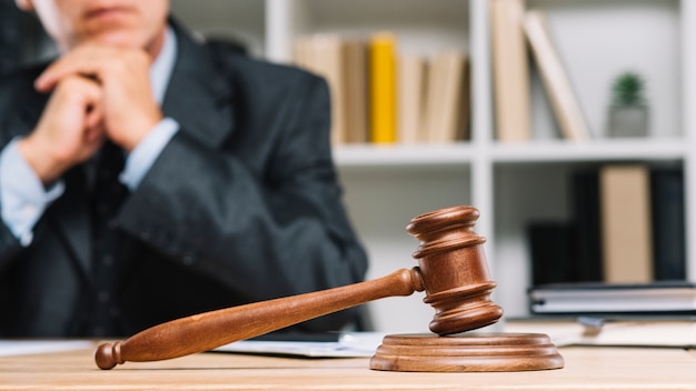 Advogado masculino sentado atrás do martelo do juiz na mesa de madeira