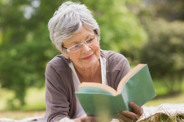 Ältere Frau, die ein Buch am Park liest