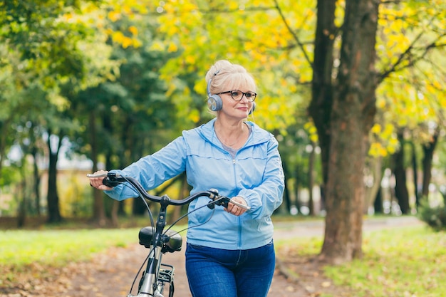 ältere Frau, die im Park mit einem Fahrrad geht