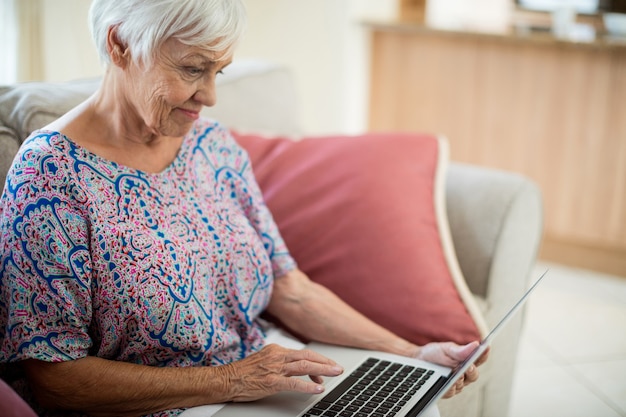 Ältere frau, die laptop im wohnzimmer zu hause benutzt