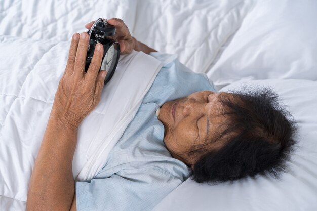 ältere Frau im Bett, das Snoozeknopf auf Morgenwecker drückt