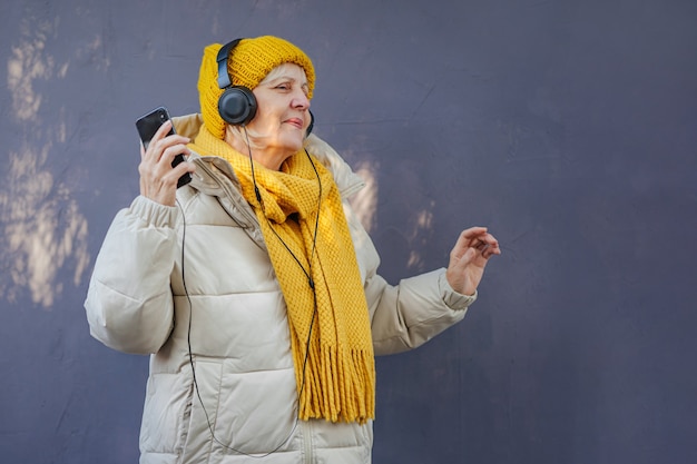 ältere Frau in stylischer Oberbekleidung, die Musik über Kopfhörer hört und tanzt