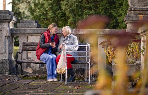 Foto Ältere frau mit gehgestell und pflegekraft im freien, die auf einer bank im park sitzt, coronavirus-konzept.