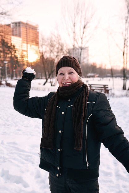 ältere Frau mit Hut und sportlicher Jacke beim Schneeballschießen im Schneewinterpark