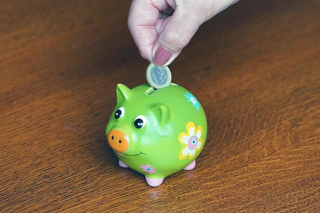 Ältere Frau spart Geld Nahaufnahme der Hand einer älteren Frau, die eine Münze in ein Sparschwein steckt
