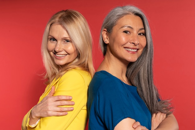 Foto Ältere frauen posieren rücken an rücken und lächeln vor einem roten hintergrund