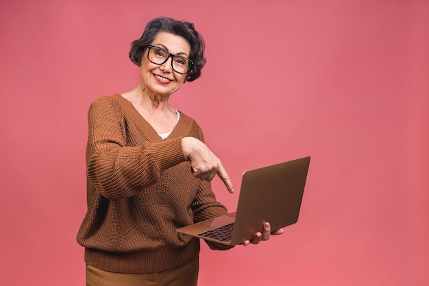 Foto Ältere gealterte geschäftsfrau mit laptop großmutter getrennt über rosa hintergrund