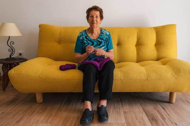 Foto Ältere kaukasische frau, die lächelnd in die kamera schaut, sitzt auf einem gelben sofa