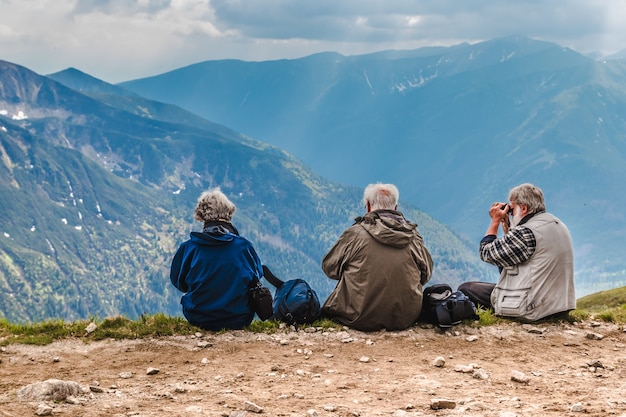 ältere menschen mit rucksäcken sitzen auf dem boden hoch in den bergen
