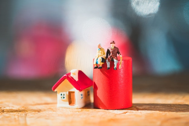 Foto Ältere miniaturmenschen, die auf rotem holzblock mit minihaus sitzen, das als arbeitsrente und familienkonzept verwendet
