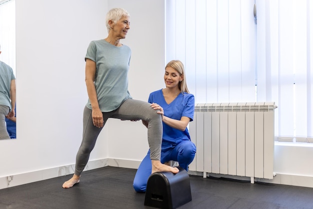 Foto Ältere patientin in der physiotherapie macht körperliche übungen mit ihrem therapeuten, die beinphysiotherapie für ältere frauen zur behandlung von osteoarthritis und nervenschmerzen im bein durchführt