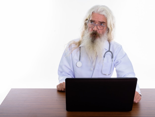 älterer bärtiger Mannarzt, der Brillen trägt, während Laptop verwendet wird