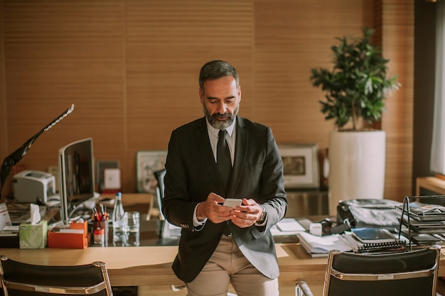 Älterer Geschäftsmann unter Verwendung des Handys und Arbeiten im modernen Büro