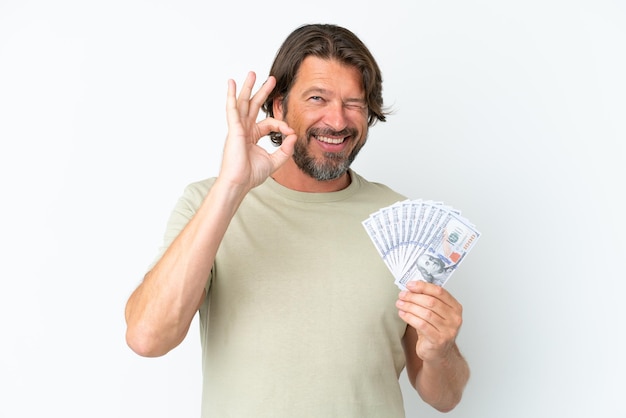 Älterer holländischer Mann, der viel Geld nimmt, isoliert auf weißem Hintergrund, der ein OK-Zeichen mit den Fingern zeigt