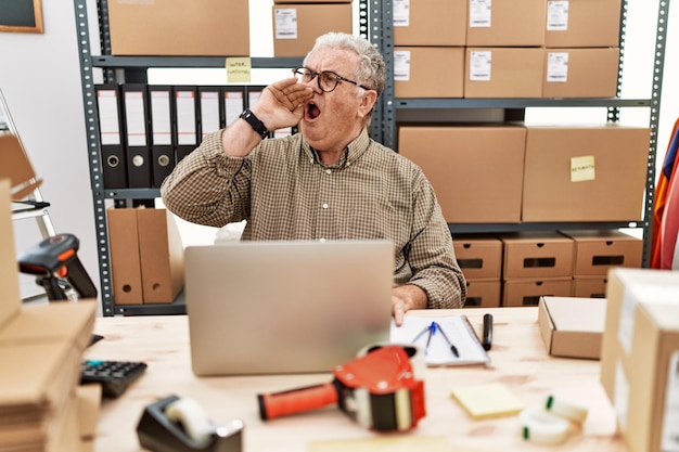 Älterer kaukasischer Mann, der im E-Commerce von Kleinunternehmen arbeitet, mit Laptop, der laut schreit und schreit, um mit der Hand auf dem Mund Kommunikationskonzept zur Seite zu stehen