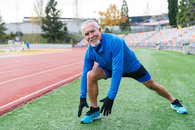 älterer kaukasischer Mann erstreckt sich auf einer athletischen Strecke in blauer Sportbekleidung