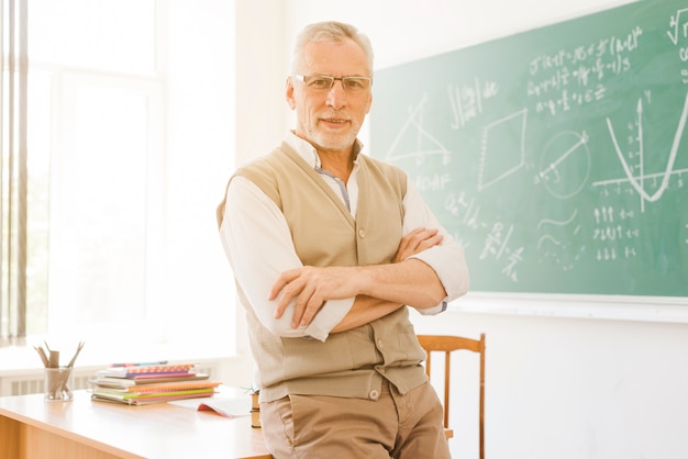 Älterer Lehrer, der nahen Schreibtisch im Klassenzimmer steht