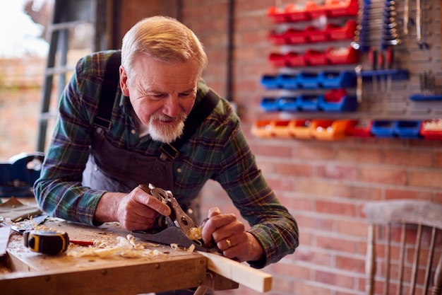 Älterer männlicher Zimmermann in der Garagenwerkstatt, der Stück Holz hobelt