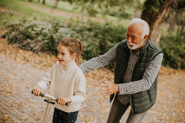 Älterer Mann bringt seiner Enkelin bei, wie man Tretroller im Park fährt