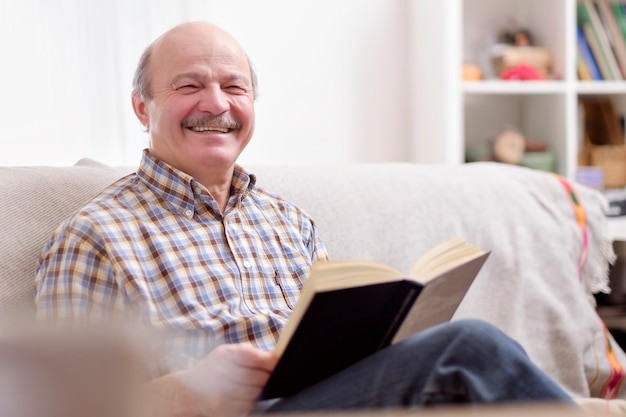 Älterer Mann, der ein Buch auf seinem Sofa liest