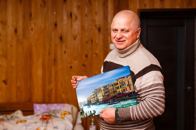 älterer Mann, der eine Fotoleinwand in einem Holzhaus hält