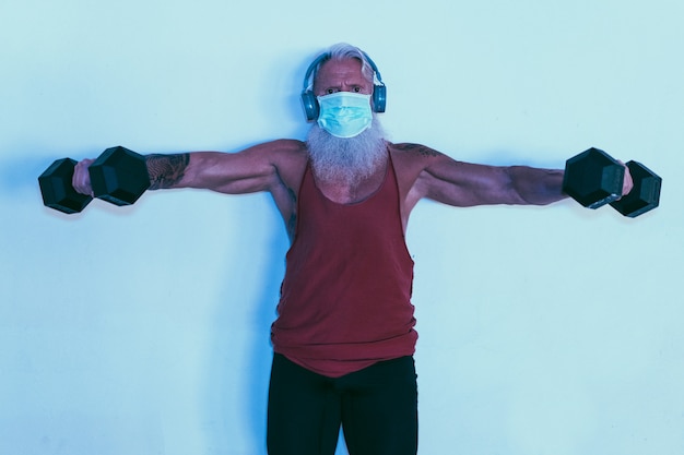 Älterer mann, der sporttraining mit hanteln beim tragen der gesichtsschutzmaske tut
