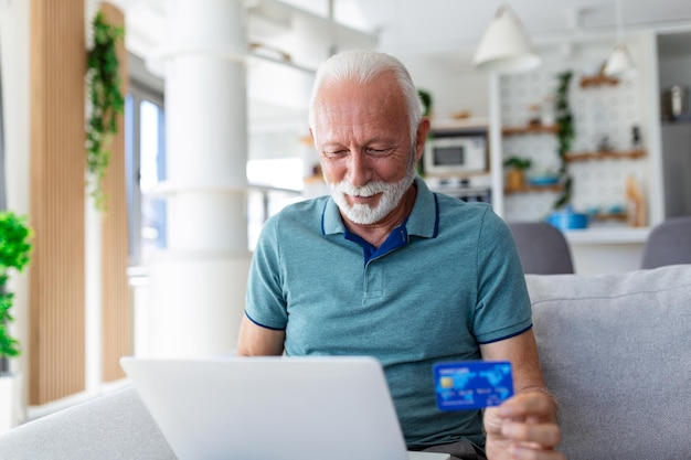 Älterer mann mit laptop, der eine kredit- oder debitkarte aus kunststoff hält