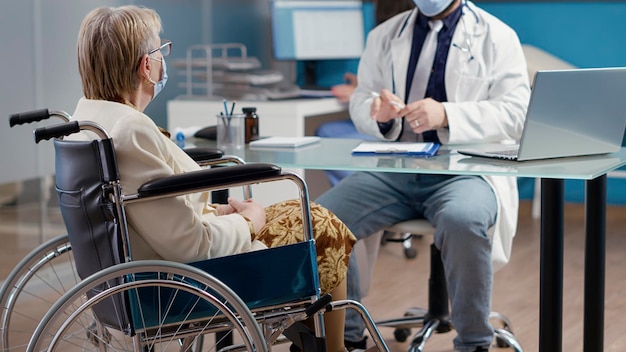 Älterer Patient mit körperlicher Behinderung, der beim Kontrolltermin im Kabinett mit dem Arzt spricht. Ältere Frau im Rollstuhl, die medizinische Behandlung erhält, um bei der Rehabilitation zu helfen.