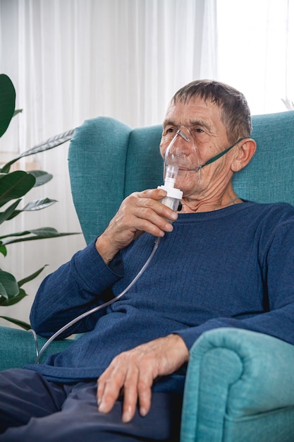 Älterer Senior sitzt in einem Sessel mit einer Sauerstoffmaske in Quarantäne