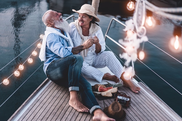 Älteres paar, das mit champagner auf einem segelboot während der sommerferien jubelt