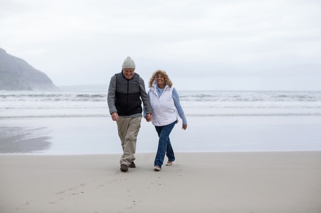 Älteres Paar, das mit Händchenhalten am Strand geht