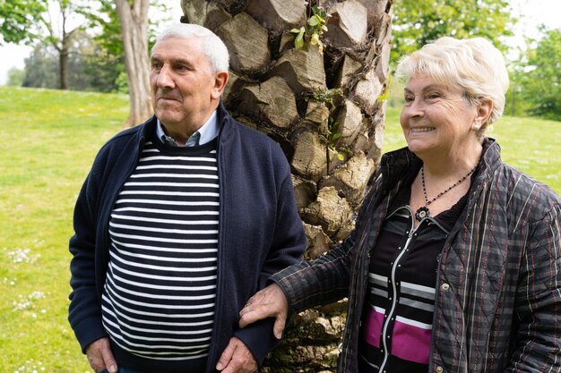 Älteres paar im park, das für die kamera posiert, die zur seite schaut ältere frau, die den arm des mannes hält