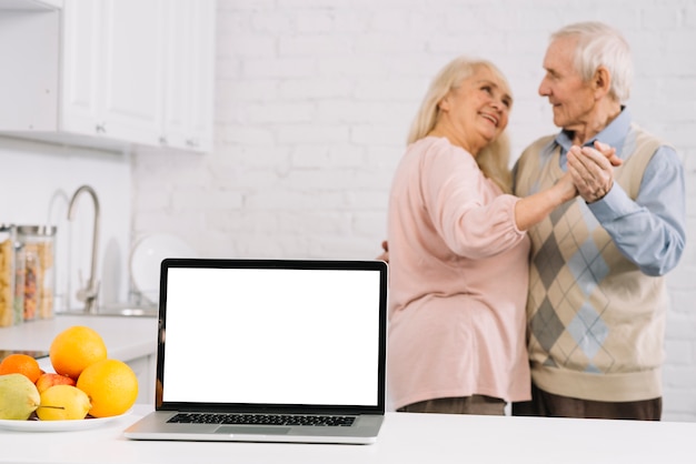 Foto Älteres paartanzen hinter laptop in der küche