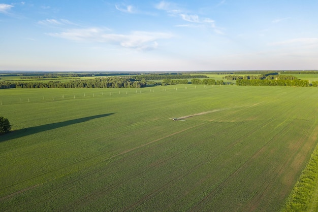 Aérea de um trator agrícola em um campo verde durante a pulverização e irrigação com pesticidas e toxinas