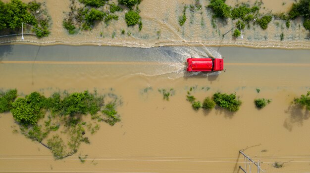 Aerial Draufsicht auf das Dorf und die Landstraße mit einem roten Auto überflutet