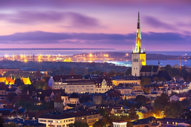 Aerial Stadtbild mit mittelalterlicher Altstadt beleuchtet in Abenddämmerung und St. Olaf Baptist Church Meer und Hafen in Tallinn Estland