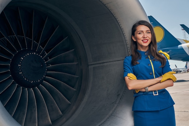 Foto aeromoça de braços cruzados encostada no motor turbofan