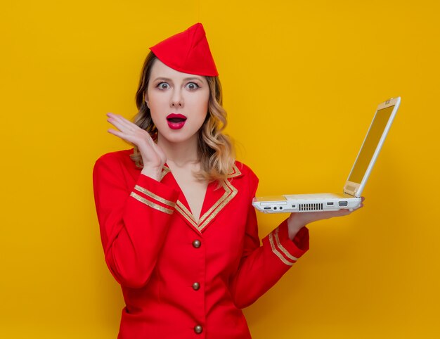 Aeromoça vestindo em uniforme vermelho com computador portátil