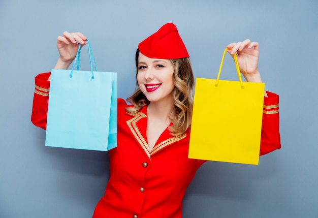 Aeromoça vestindo uniforme vermelho com sacolas de compras.