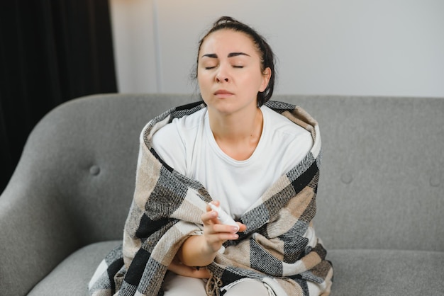 Foto aerosol nasal en la mano de una joven enferma sentada en el sofá síntomas y tratamiento de la rinitis alérgica